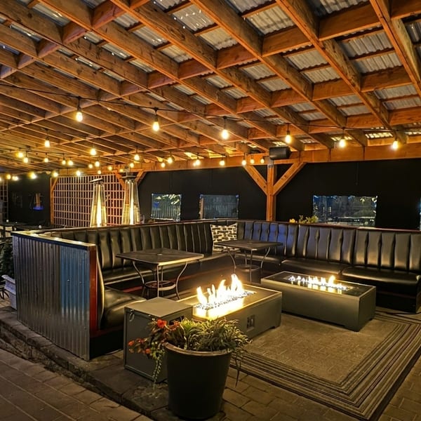 An inviting outdoor patio at night, featuring string lights, fire pits, and comfortable seating.