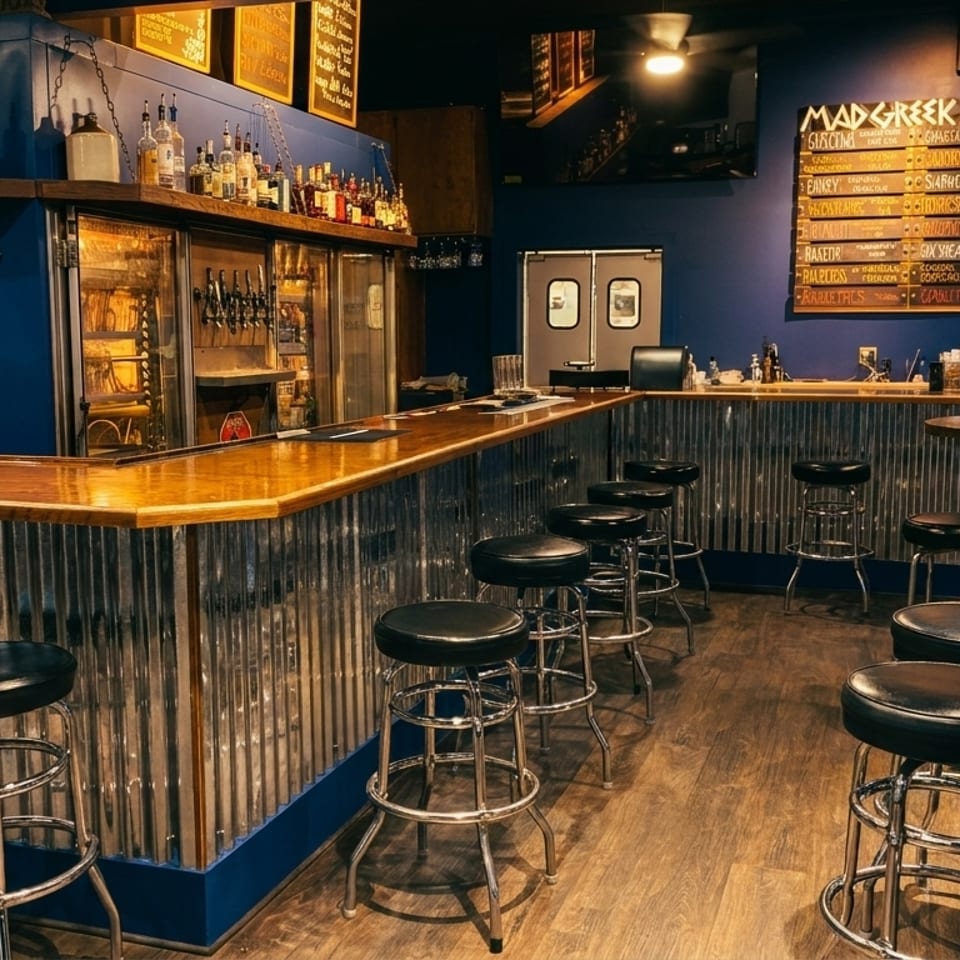 Interior of a bar with a long wooden counter, black stools, and a menu board on a blue wall.