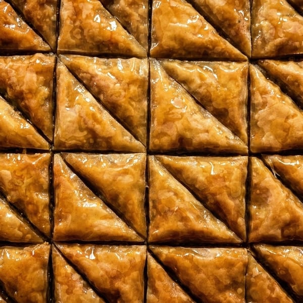 Close-up of golden-brown, triangular baklava pastries arranged in a grid, glistening with syrup.